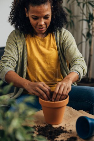 Photo for Closeup view of a happy multiracial woman filling a flowerpot with dirt - Royalty Free Image