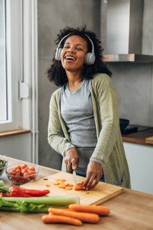 Foto de Mujer multiracial canta mientras cocina en la cocina. - Imagen libre de derechos