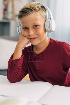 Foto de Un joven lindo con auriculares está escuchando la clase en línea y mirando a la cámara. - Imagen libre de derechos