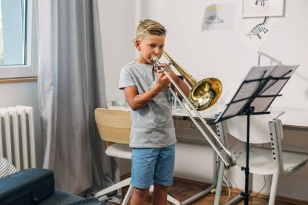 Téléchargez les photos : Un garçon joue au trombone à la maison. - en image libre de droit
