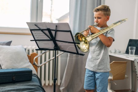 A Caucasian boy practicing trombone at home.