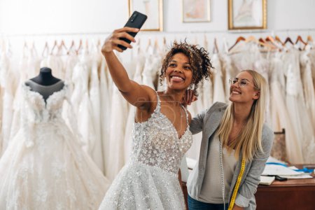 Photo for A beautiful Multiracial bride takes a photo with a tailor in a bridal salon. - Royalty Free Image