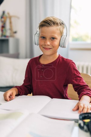 Photo for Cute Caucasian boy with headset is studying at home. - Royalty Free Image