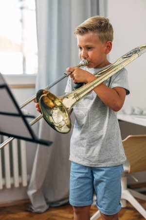 Téléchargez les photos : Jeune garçon lit des notes et joue un trombone. - en image libre de droit