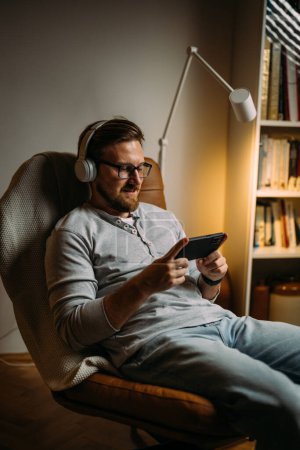 Photo for Man with headphones using cellphone in the evening at home - Royalty Free Image