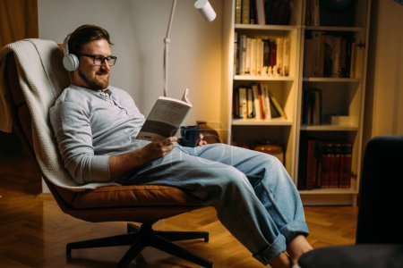 Foto de Caucásico hombre ama relajarse con un buen libro en la noche en casa. - Imagen libre de derechos
