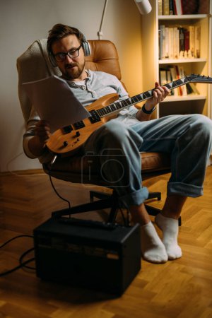 Téléchargez les photos : Vue de face d'un homme de race blanche lisant des notes et jouant de la guitare. - en image libre de droit
