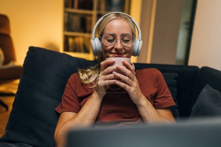 Téléchargez les photos : Femme heureuse boire du café tout en utilisant un ordinateur portable. - en image libre de droit