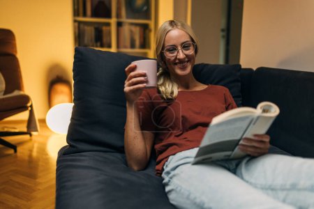 Téléchargez les photos : Femme souriante lisant le livre le soir. - en image libre de droit