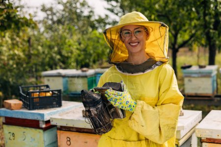 Happy female beekeeper holding a smoker.