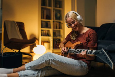 Photo for Beautiful Caucasian woman is playing an electric guitar at home. - Royalty Free Image