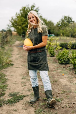 Téléchargez les photos : Vue de face d'une jeune jardinière joyeuse tenant une citrouille. - en image libre de droit