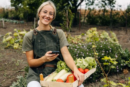 Téléchargez les photos : Portrait d'une jeune femme heureuse récoltant des légumes dans le jardin. - en image libre de droit