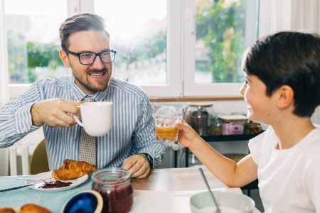 Téléchargez les photos : Heureux père et fils profitant du petit déjeuner ensemble un jour de travail. - en image libre de droit