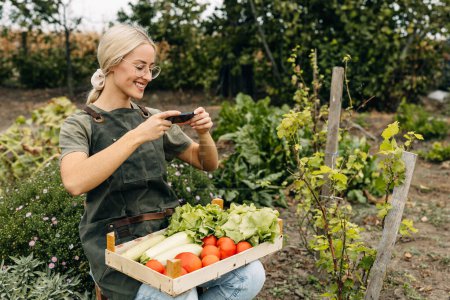 Téléchargez les photos : Heureuse jardinière prenant une photo de légumes de son jardin. - en image libre de droit