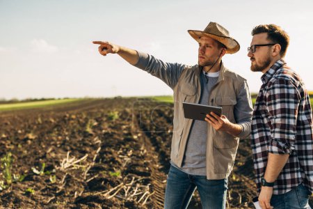 Photo for Two man standing in farmland with a tablet and monitoring the field. - Royalty Free Image