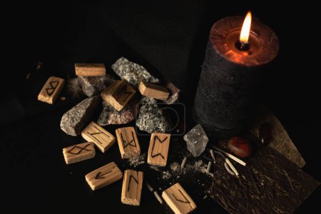 Photo for Wooden runes on a dark background with a candle and amber stones, for a magical ritual - Royalty Free Image