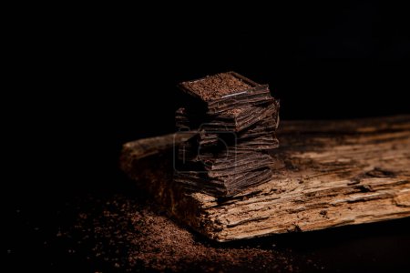 Téléchargez les photos : Morceaux de chocolat noir reposent les uns sur les autres, sur une assiette en bois - en image libre de droit