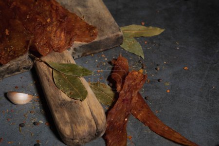 Deux morceaux de délicieux jerky sur une planche de bois et un fond de tempête avec de l'ail et des épices.