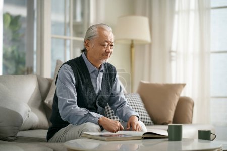 Téléchargez les photos : Triste asiatique senior homme assis sur canapé dans salon à la maison - en image libre de droit