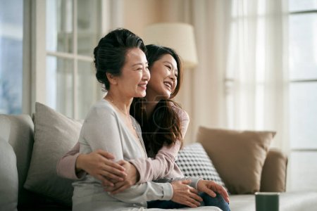 Foto de Amoroso asiático adulto hija sentado en sofá en casa abrazando senior madre feliz y sonriente - Imagen libre de derechos
