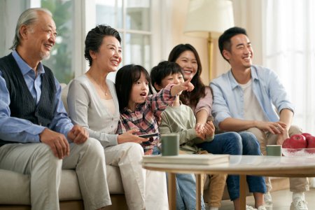 Photo for Three generation asian family sitting on couch at home watching tv together happy and smiling - Royalty Free Image