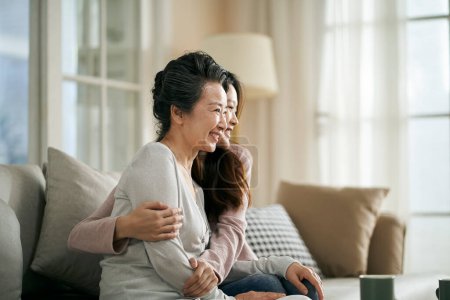 Téléchargez les photos : Portrait de mère âgée asiatique et fille adulte assis sur le canapé à la maison heureux et souriant - en image libre de droit