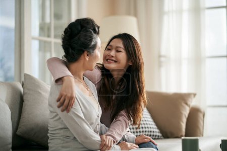 Téléchargez les photos : Asiatique adulte fille et senior mère assis sur canapé à la maison avoir une agréable conversation - en image libre de droit