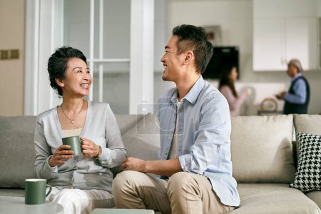 Photo for Asian adult son and senior mother sitting on couch in living room at home having a pleasant conversation - Royalty Free Image