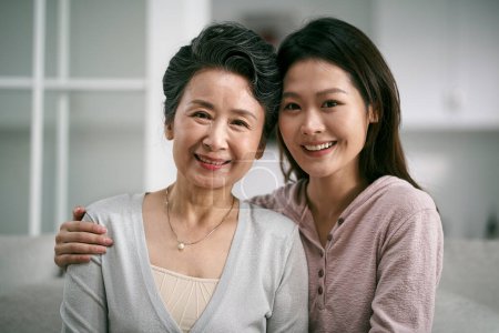 Foto de Retrato de asiático anciano madre y adulto hija sentado en sofá en casa feliz y sonriente - Imagen libre de derechos