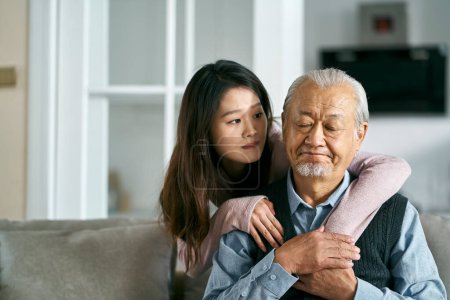 Photo for Sad senior asian father sitting on couch in living room at home consoled by adult daughter - Royalty Free Image