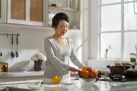 Foto de Senior asian woman standing in modern kitchen at home getting ready to prepare food - Imagen libre de derechos