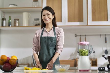 Photo for Happy young asian woman housewife standing in kitchen looking at camera smiling - Royalty Free Image