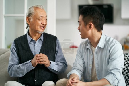 Photo for Senior asian father having a good time sitting on couch at home chatting with adult son - Royalty Free Image