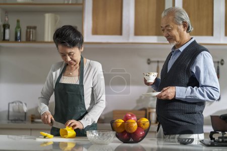 Photo for Loving senior asian couple chatting talking conversing in kitchen at home while preparing food - Royalty Free Image