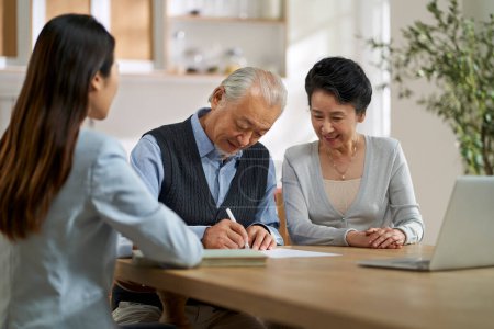 Téléchargez les photos : Senior asian couple signing an agreement in front of a saleswoman at home - en image libre de droit