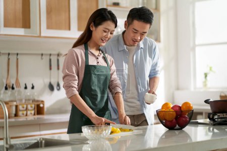 Photo for Loving young asian couple chatting talking conversing in kitchen at home while preparing food - Royalty Free Image