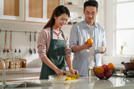 Photo for Loving young asian couple chatting talking conversing in kitchen at home while preparing food - Royalty Free Image