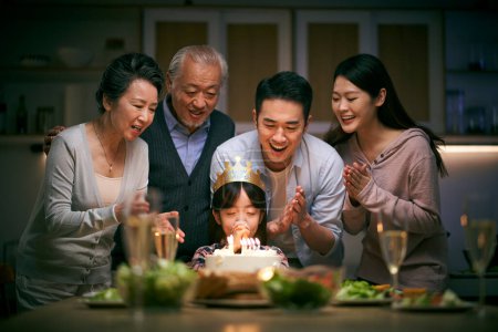 Téléchargez les photos : Petite fille asiatique faire un vœu tandis que la famille de trois générations fête son anniversaire à la maison - en image libre de droit