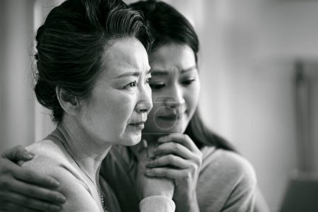Photo for Grieving senior asian mother and adult daughter holding hands, black and white - Royalty Free Image