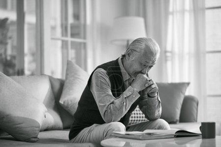 Téléchargez les photos : Asiatique senior homme assis sur canapé penser dans salon à la maison, noir et blanc - en image libre de droit