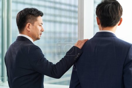 Téléchargez les photos : Deux asiatiques hommes d'affaires debout par la fenêtre bavarder parler - en image libre de droit
