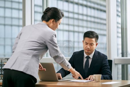 Téléchargez les photos : Asiatique chef d'entreprise examen document papier rapport soumis par assistant féminin dans bureau moderne - en image libre de droit