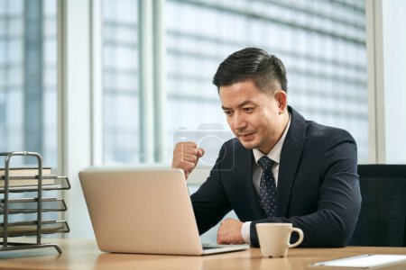 Foto de Mediados de adulto asiático hombre de negocios sentado en el escritorio de trabajo en la oficina utilizando ordenador portátil - Imagen libre de derechos
