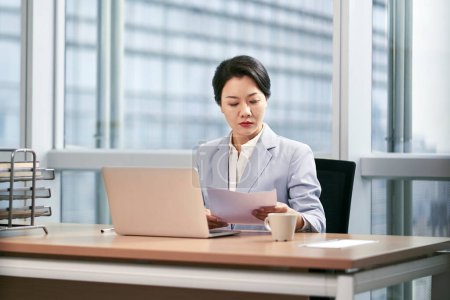 Téléchargez les photos : Jeune femme d'affaires asiatique travaillant dans un bureau moderne à l'aide d'un ordinateur portable - en image libre de droit