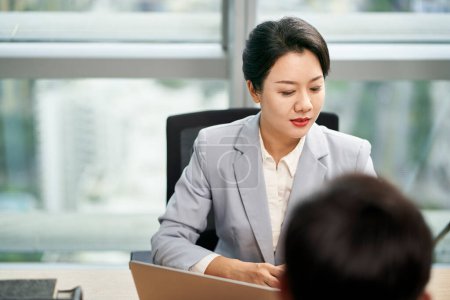 Téléchargez les photos : Jeune asiatique femme d'affaires gestionnaire assis au bureau parler à un collègue masculin dans le bureau moderne - en image libre de droit