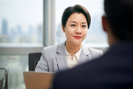 Photo for Young asian businesswoman female manager sitting at desk talking to male colleague in modern office - Royalty Free Image