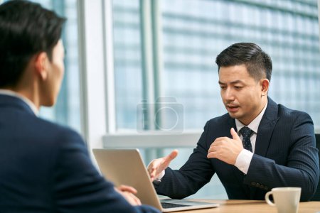 Téléchargez les photos : Deux hommes d'affaires asiatiques assis au bureau face à face dans le bureau moderne ayant une discussion - en image libre de droit