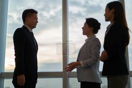 Photo for Three asian business people standing by the window in office having a conversation - Royalty Free Image
