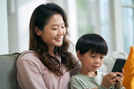 Photo for Young asian woman mother sitting on family couch keeping company with five-year-old son - Royalty Free Image